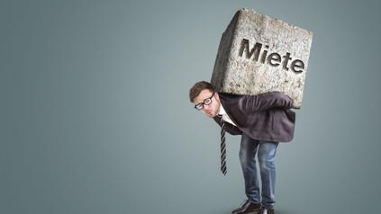 Mann trägt Felsbrocken mit der Aufschrift "Miete" auf seinem Rücken