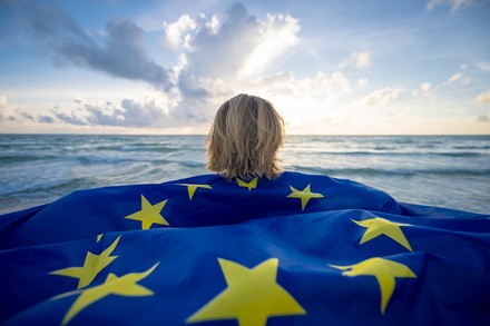 Eine Frau mit EU-Flagge schaut aufs Meer