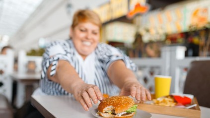 Dicke Frau greift nach angebissenem Burger