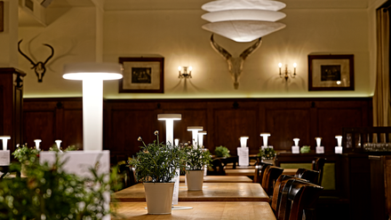 Rustikal modern eingerichteter Gastraum mit Kräutertöpfen auf den Tischen und Geweihen an der Wand