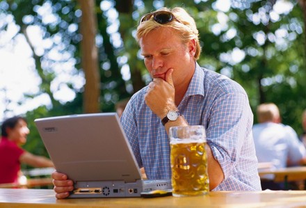 Mann sitzt mit Bier an Laptop