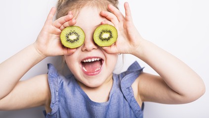 Ein lachendes Kind hält sich zwei Kiwischeiben vor die Augen