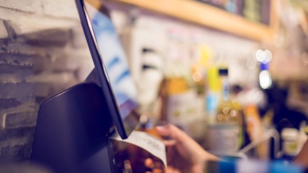 Verschwommenes Bild einer Registrierkasse in einer Bar oder einem Café, mit der ein Angestellter einen Kassenbon druckt