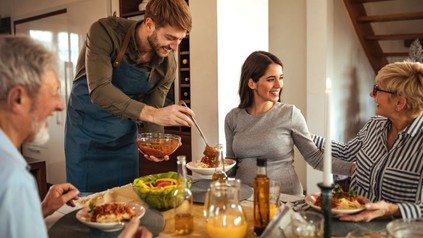 Mann serviert in seiner Wohnung Freunden ein Essen
