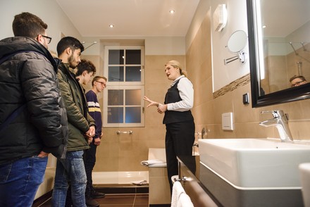 Hotel-Mitarbeiterin erklärt Jugendlichen die Reinigungsarbeit in einem Badezimmer