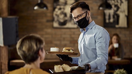 Kellner mit Handschuhen und Mund-Nasen-Schutz bedient einen Gast