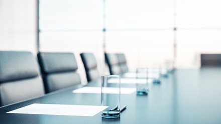 Leerer Konferenztisch vor einer Glaswand mit Gläsern und Notizblättern