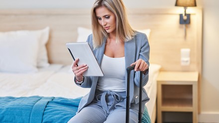 Mit einer digitalen Gästemappe haben Gäste das wichtigste über das Hotel und die Umgebung immer griffbereit. (Foto: © Kamil – stock.adobe.com)
Junge Frau sitzt auf dem Hotelbett und checkt die digitale Gästemappe