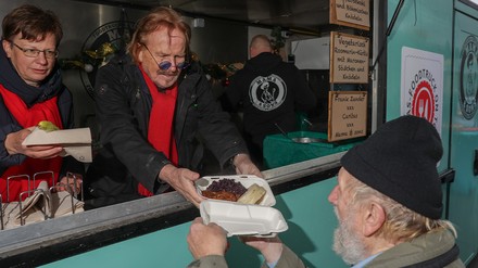 Frank Zander (Mitte) und Ulrike Kostka (links) von der Caritas verteilen zum Start von „Zanders Weihnachtstour“ eine warme Mahlzeit an einen Bedürftigen. (Foto: © picture alliance/dpa | Jörg Carstensen)
Frank Zander (Mitte) und Ulrike Kostka (links) von der Caritas