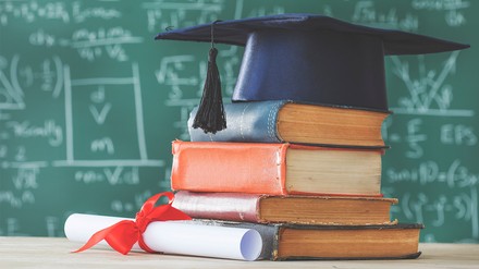 Die Cornell Hotel Society fördert den Nachwuchs mit einem Stipendium und vergibt Kurse an der Cornell Nolan School of Hotel Administration. (Foto: © sebra/stock.adobe.com)
Dicke Lehrbücher liegen auf einem Tisch, darauf liegt ein Stipendiatenhut. Im Hintergrund steht eine vollgeschriebene Tafel.