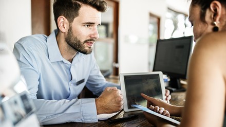 Die Bundesregierung prüft derzeit die Möglichkeiten für eine vollständige Digitalisierung der Hotelmeldepflicht. (Foto: © Rawpixel Ltd./stock.adobe.com)
Ein Hotelmitarbeiter an der Rezeption zeigt einer jungen Frau etwas auf dem Tablet