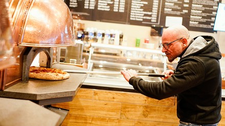 Francesco Ialazzo, Weltmeister der Pizzabäcker, schiebt im Café Planken in der Innenstadt eine Pizza in einen Steinofen. (Foto: © picture alliance/dpa | Uwe Anspach)
Pizza-Weltmeister backt Pizza.