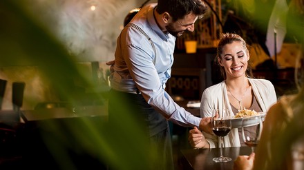 Wer die Food&Beverage Trends des Jahres 2023 kennt, der kann bei Gästen und Mitarbeitern punkten. (Foto: © BGStock72/stock.adobe)
Ein Mann bringt einer Frau Essen.