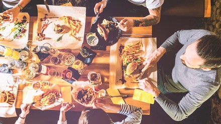 Welches sind die besten Restaurants in Deutschland? OpenTable hat auch für 2019 ein Ranking der Top 50 nach Nutzer-Bewertungen erstellt. (Foto: ©nik0.0kin/Fotolia)
Mehrere Menschen sitzen an einem gedeckten Tisch und essen zusammen Burger