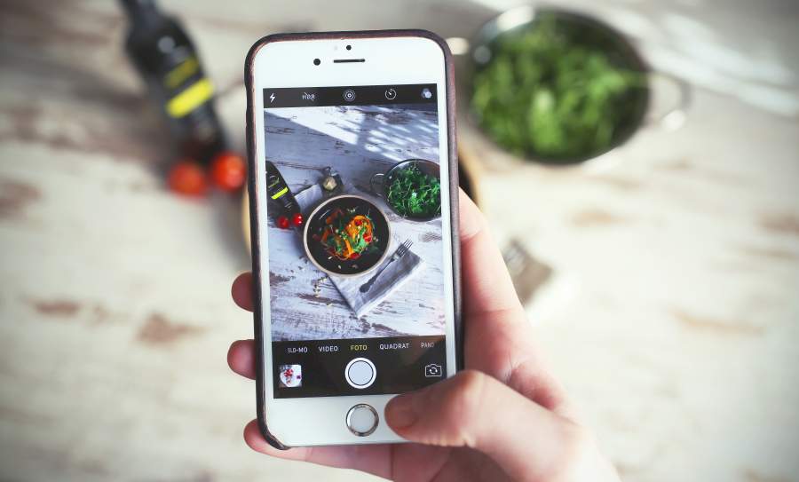 Eine Hand hält ein Smartphone auf dem ein Foto eines leckeren Salats zu sehen ist